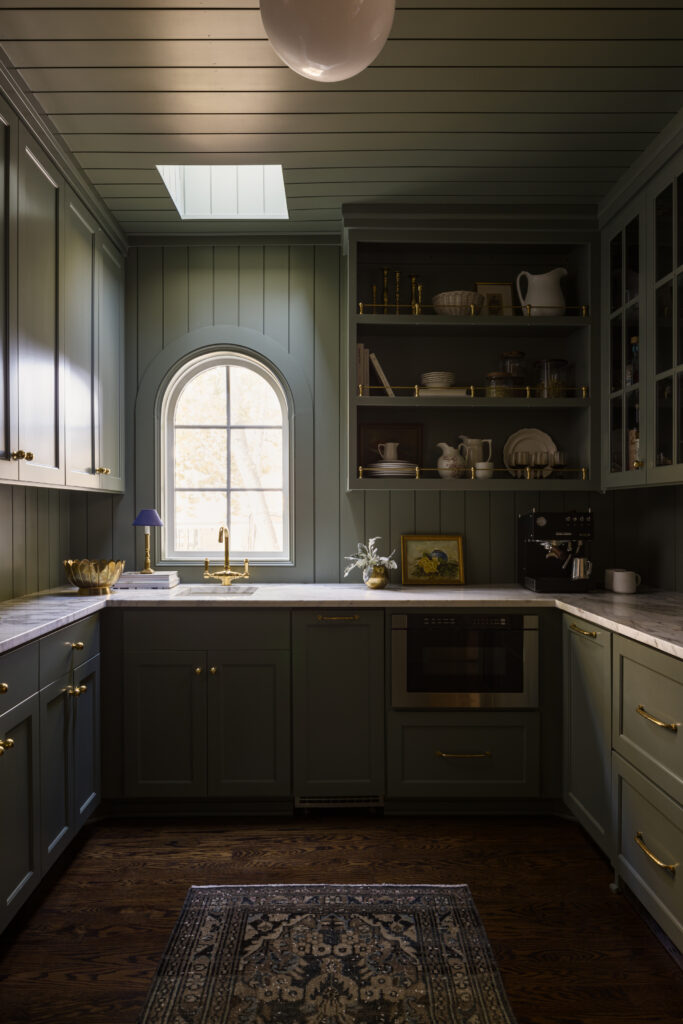 Arched window above sink in green butler's pantry.