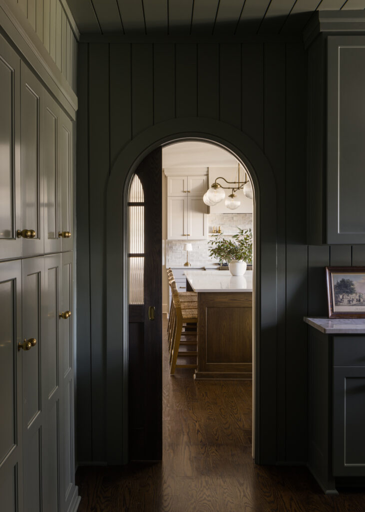 Arched pocket door in butler's pantry with shiplap walls and painted in olive green.