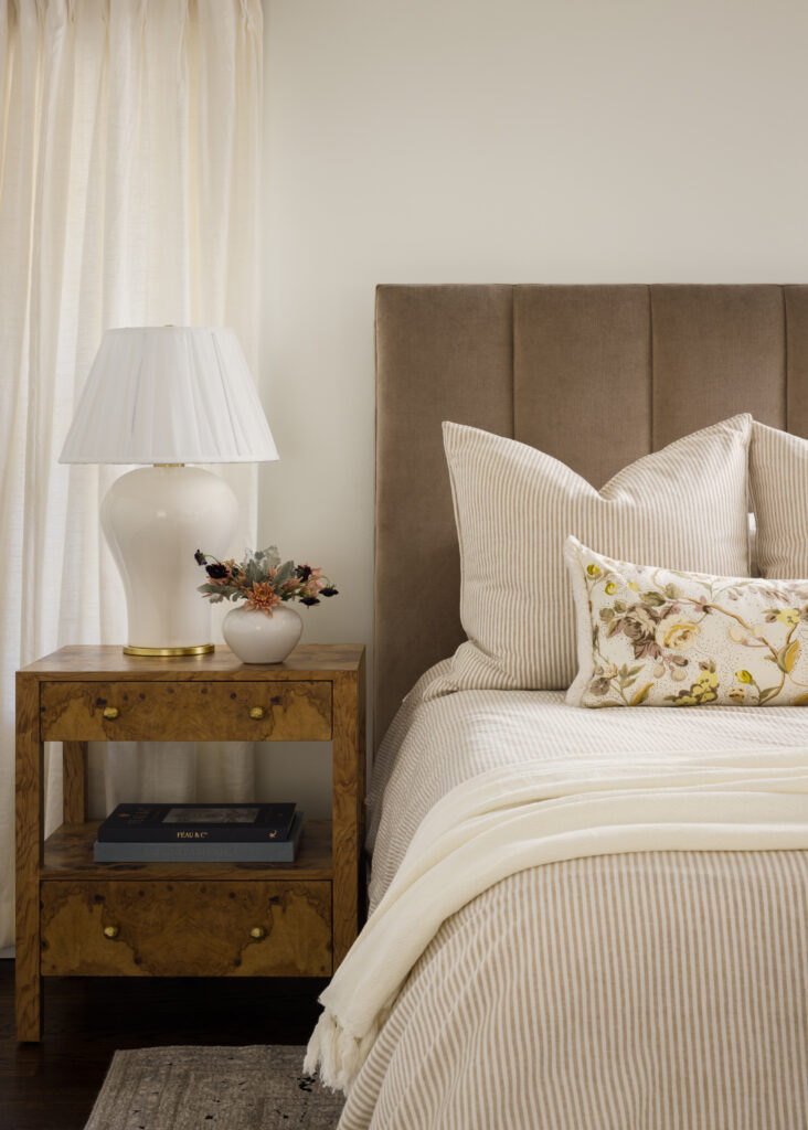 Traditional bedroom design with mushroom colored upholstered headboard and burl wood nightstand.